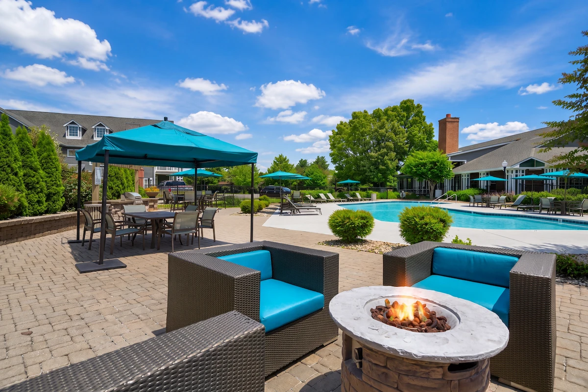 Luxurious apartment complex courtyard with inviting pool, cozy fire pit seating, and elegant outdoor dining under vibrant blue umbrellas.