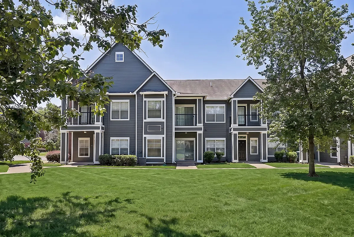 Charming two-story apartment building with modern gray siding, surrounded by lush green lawns and shaded by mature trees.