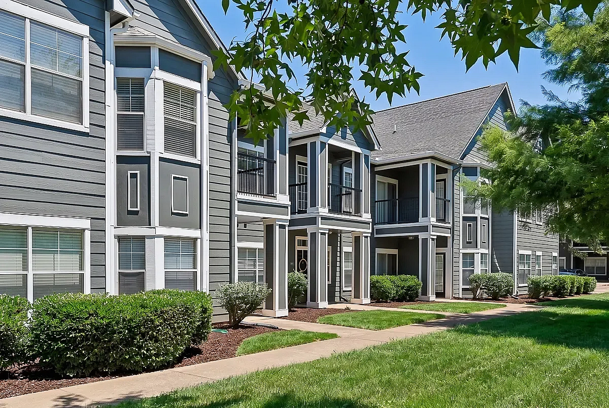 Charming modern apartment building with elegant gray siding, surrounded by lush greenery and inviting pathways.