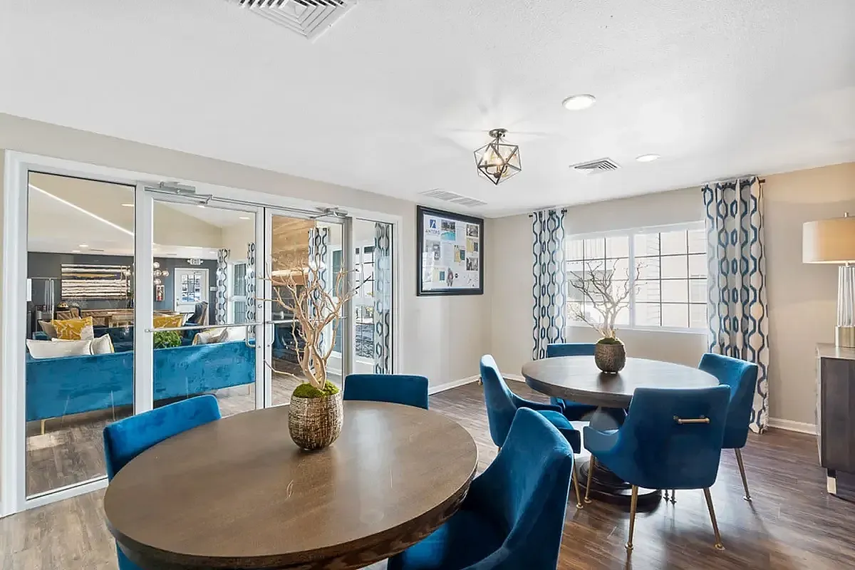 Chic and inviting seating area featuring elegant blue chairs and wooden tables, accented by stylish decor and warm lighting at Antero Apartments.