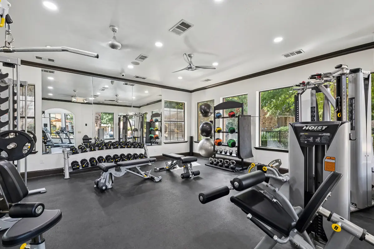 Modern fitness center with advanced gym equipment, free weights, and natural light streaming through large windows at Enclave on Golden Triangle Apartments in Fort Worth Texas