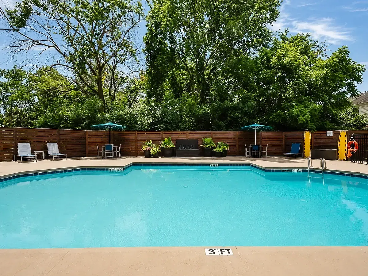 Inviting outdoor pool with comfortable lounge chairs and shaded tables surrounded by lush greenery.
