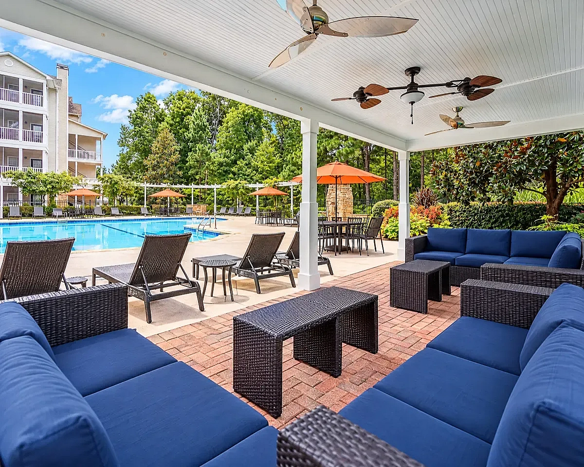 Summer Park's luxurious poolside area featuring a covered lounge with plush blue seating, surrounded by lush greenery and modern amenities.