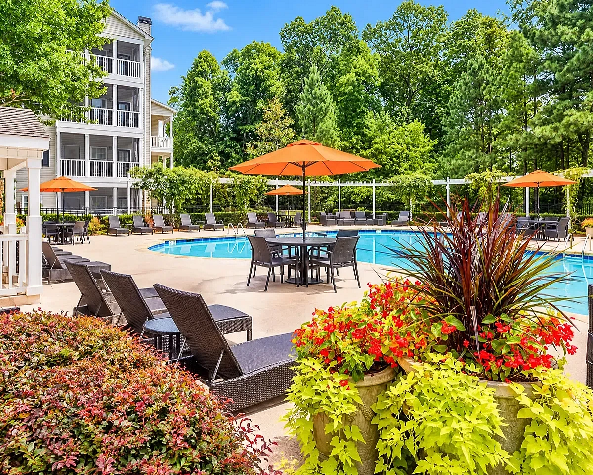 Charming outdoor pool area with lush greenery, inviting poolside loungers, and vibrant umbrellas creating a serene oasis at Summer Park Apartments.