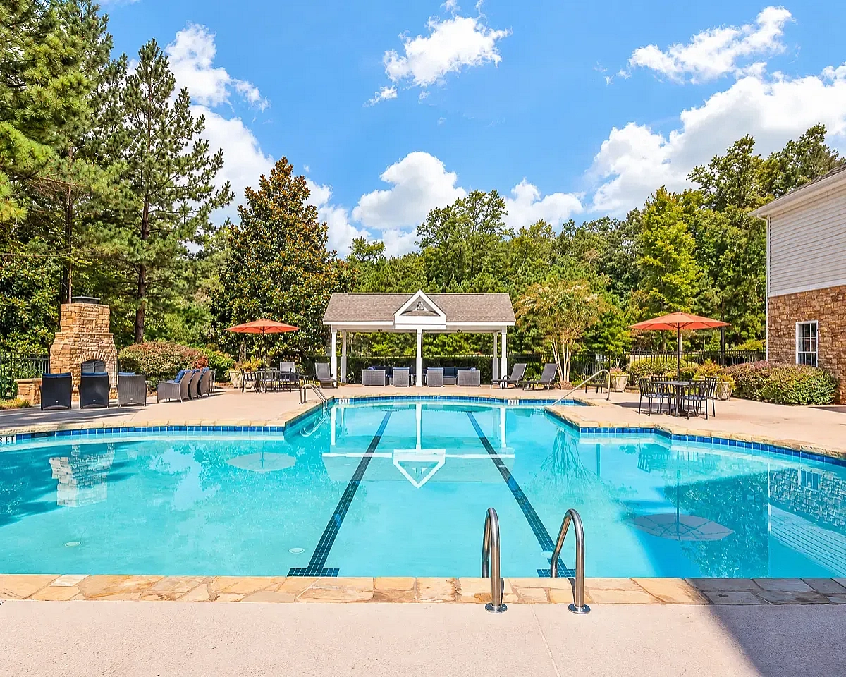 Inviting outdoor pool at Summer Park Apartments with sun loungers, cozy seating, and vibrant umbrellas set against lush greenery.