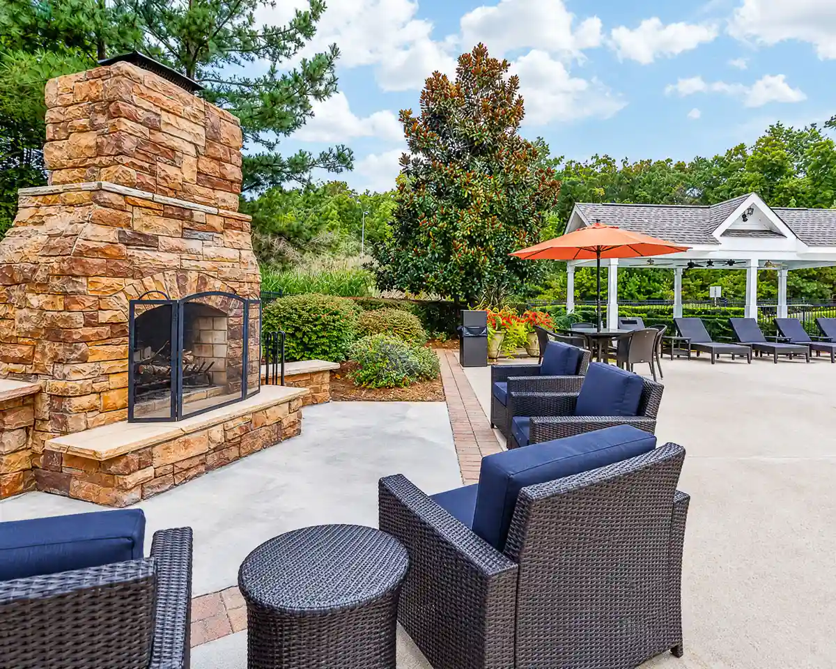 Charming outdoor patio featuring a stone fireplace, cozy wicker furniture with blue cushions, and a shaded pergola, perfect for relaxation and entertaining at Summer Park Apartments.