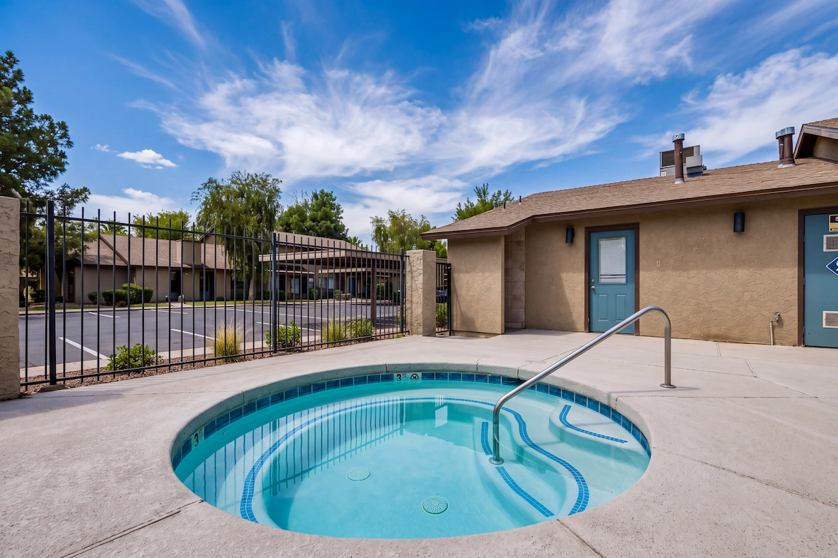 Round hot tub with entry steps and a handrail beside a fenced pool area.