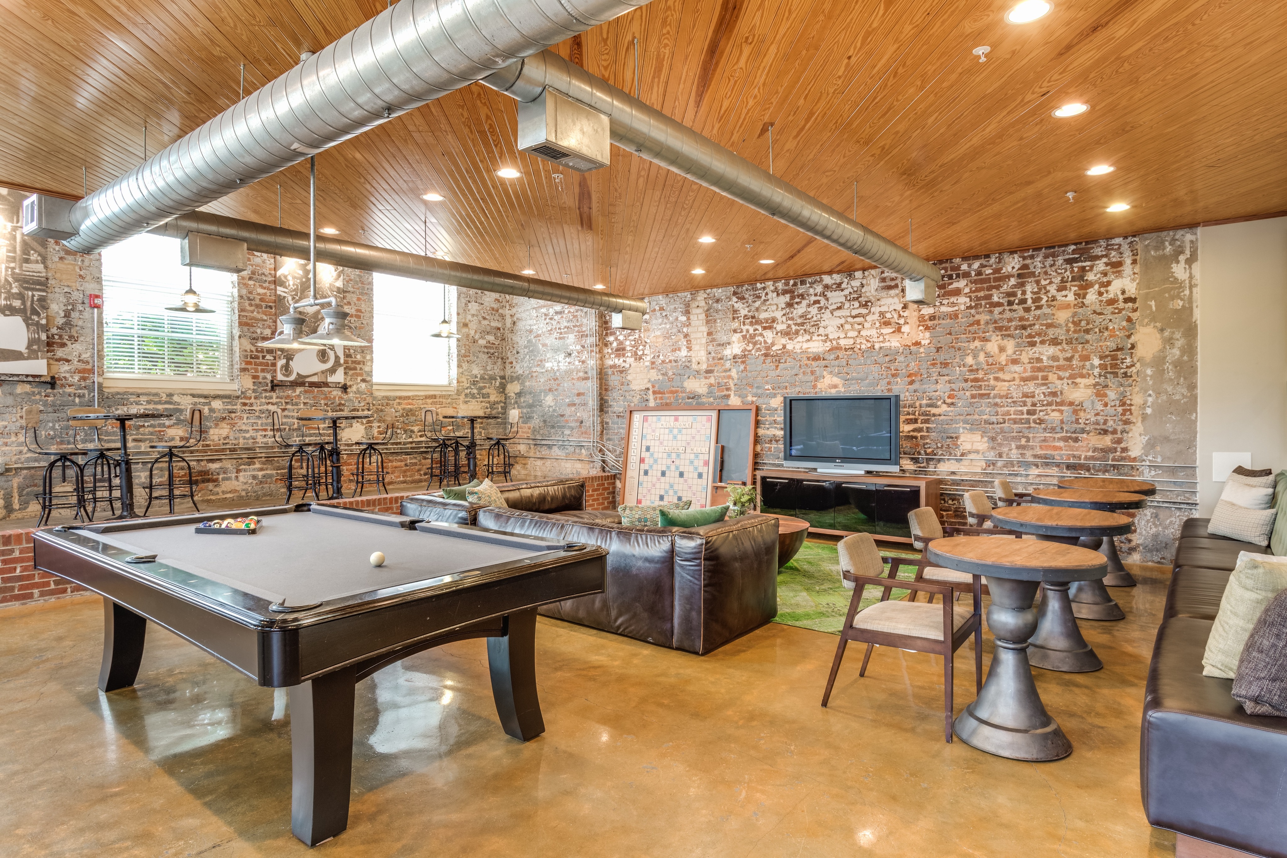View of Resident Lounge, Showing Pool Table, Sitting Areas, TV, and Mill Architecture at Alpha Mill Apartments