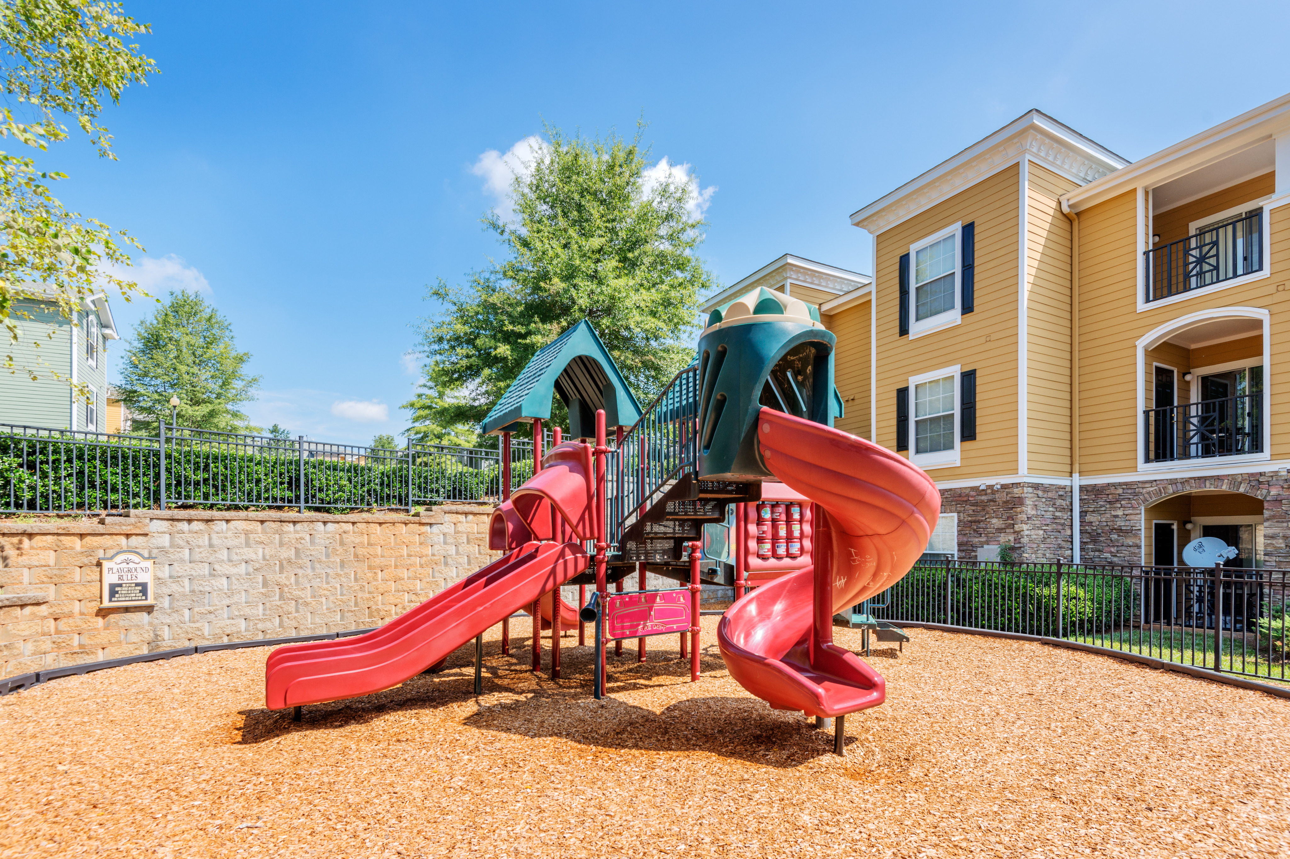 View of Children\'s Playground , Showing Fenced Landscaping, Dual Slides, Activity Stations, and Building at Cottonwood Reserve Apartments