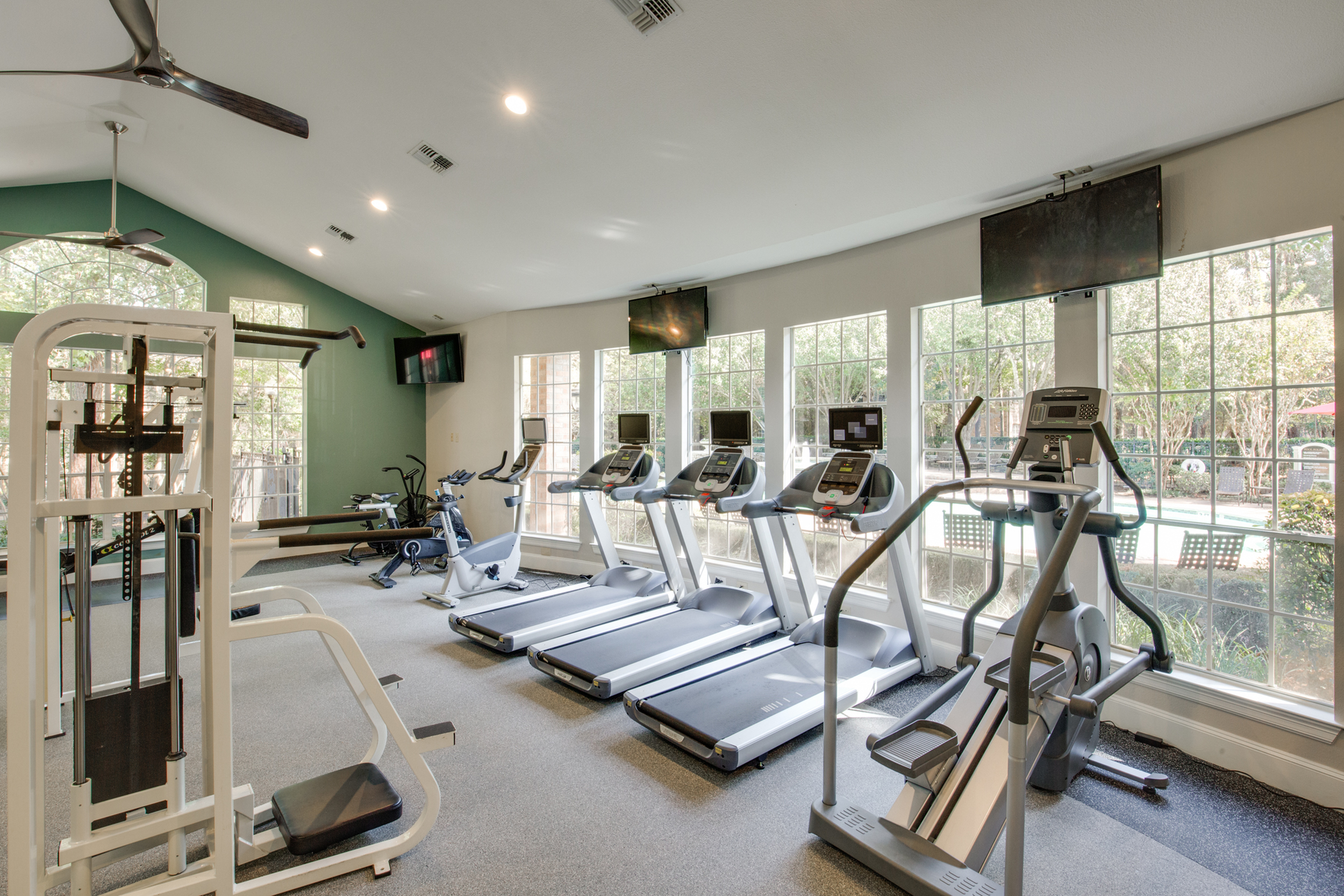 View of Fitness Center with Ceiling Fan, Cardio Machines, and Mounted Flat Screen TVs at Raveneaux Apartments