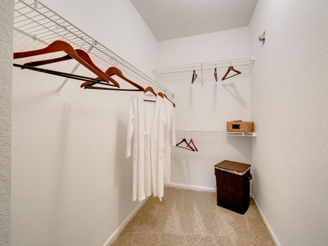 View of Classic Apartment Interior, Showing Closet with Hangers, Clothes Hanging, and Hamper at Stonebriar of Frisco Apartments