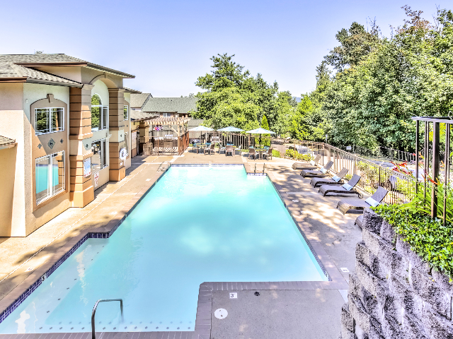 View of Swimming Pool at Scott Mountain by the Brook Apartments also showing lounge chairs, umbrella, and community clubhouse.