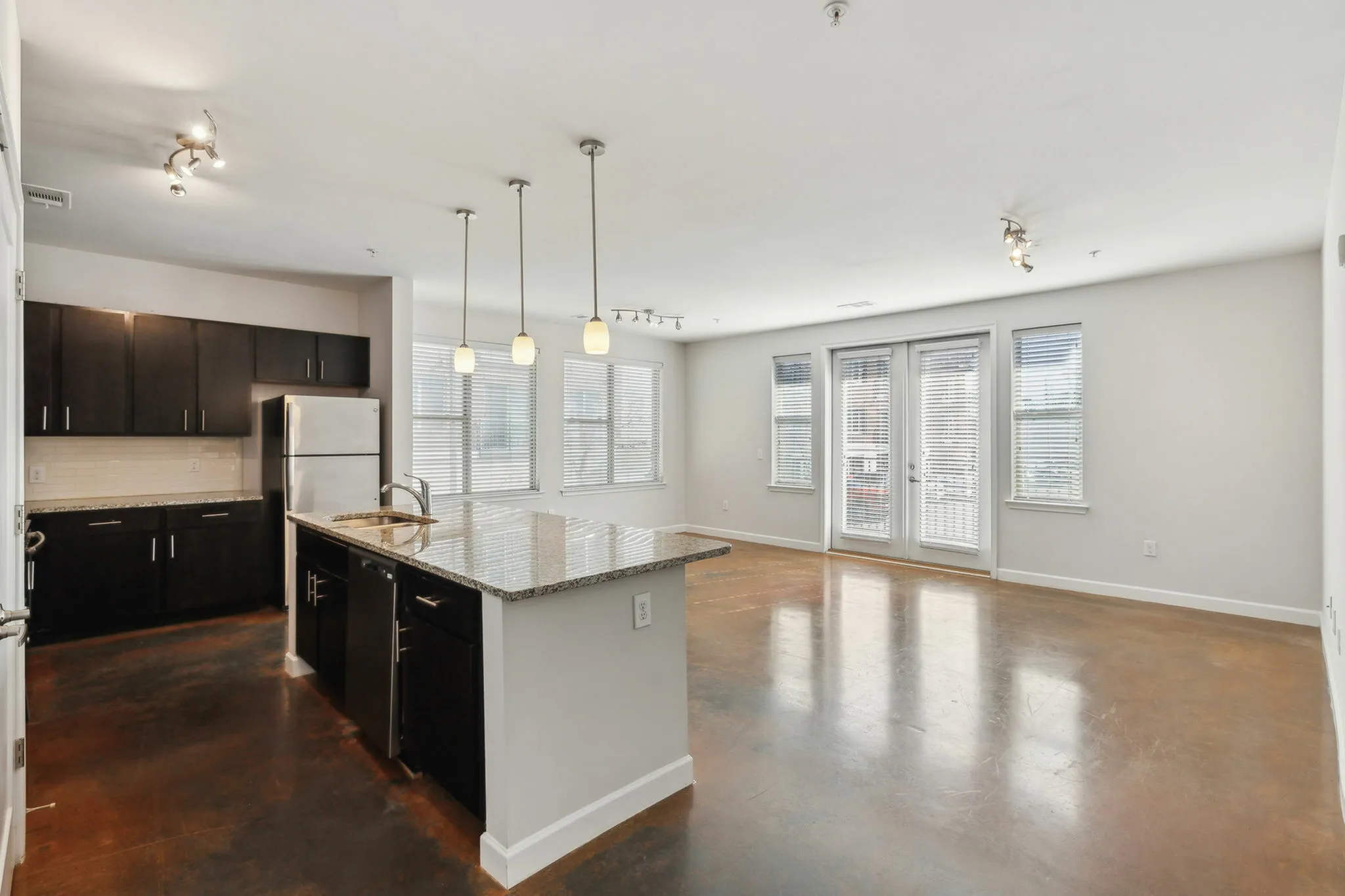 Spacious open-concept kitchen with granite countertops, sleek dark cabinets, and pendant lighting.