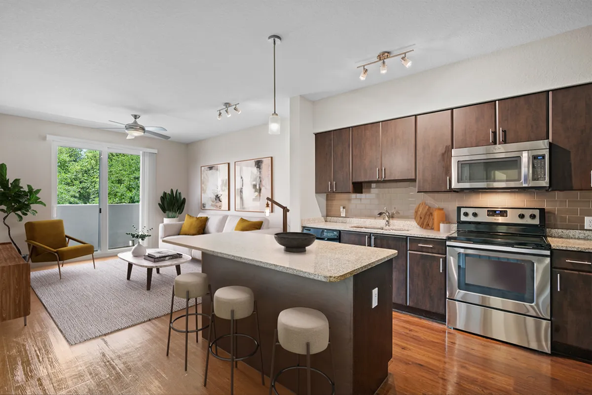 Modern open-concept living room and kitchen featuring stylish wood cabinets, stainless steel appliances, and a cozy seating area with natural light and greenery views.