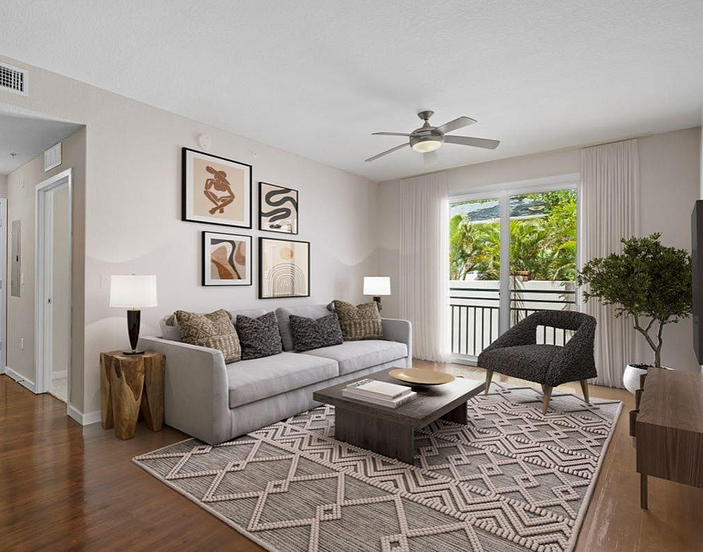 Bright and airy living room with modern decor, cozy gray sofa, elegant art pieces, and large window showcasing lush greenery outside.