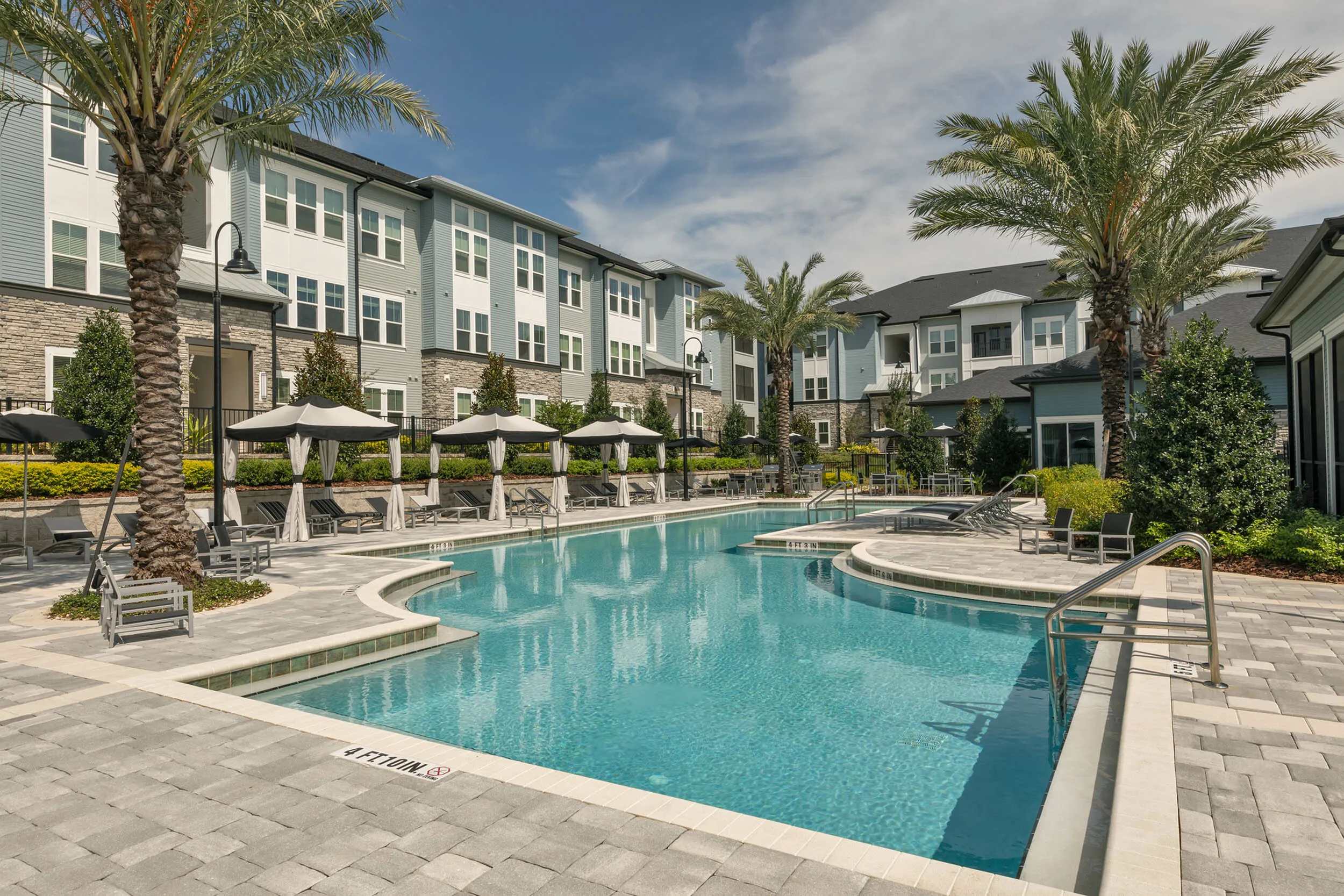 Luxurious apartment complex featuring a sparkling swimming pool surrounded by elegant lounge chairs and tropical palm trees at Cottonwood Clermont Apartments in Florida.