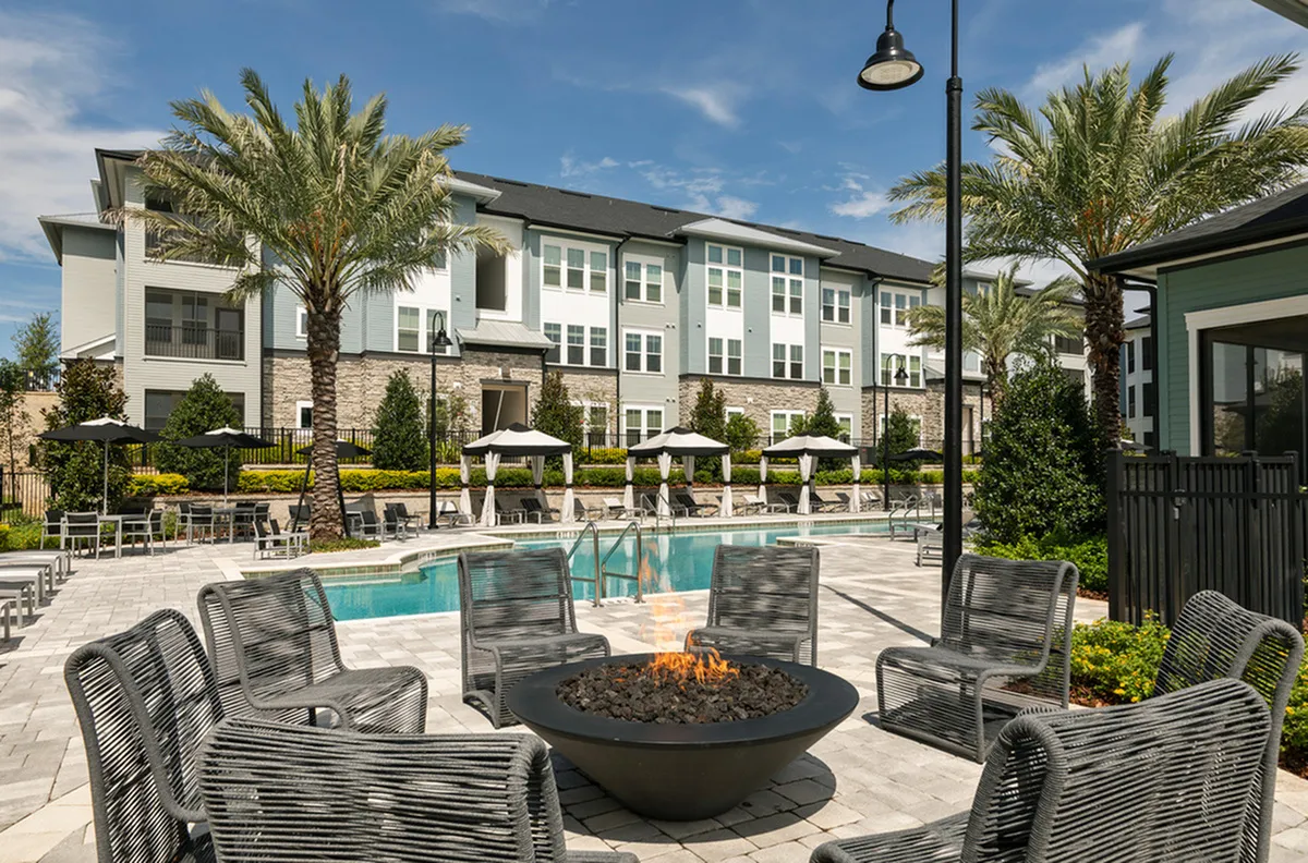 View of Firepit Lounge Cottonwood Clermont Apartments Showing Lounge Seating, Firepit, Large Palm Trees, Pool, and Community Exterior