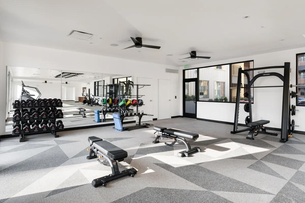 Modern fitness center at Cottonwood Highland with state-of-the-art equipment, featuring treadmills, free weights, and sleek benches in a spacious, well-lit environment.