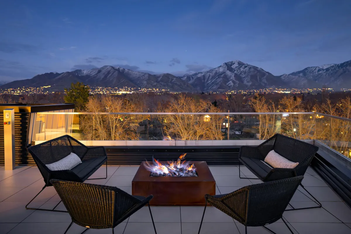 Chic rooftop terrace at Cottonwood Highland Apartments with cozy seating around a modern fire pit, offering spectacular city and mountain views at dusk.