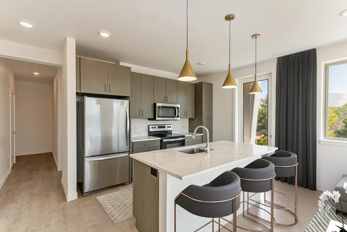 Modern kitchen at Cottonwood Highland in Millcreek with sleek stainless-steel appliances, elegant pendant lighting, and a spacious island with stylish bar stools, offering a perfect blend of functionality and sophistication.
