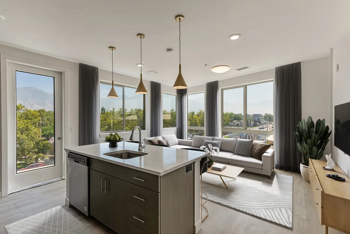 Bright and modern living space at Cottonwood Highland Apartments with panoramic windows, sleek kitchen island, and cozy seating area, ideal for relaxation and entertaining.