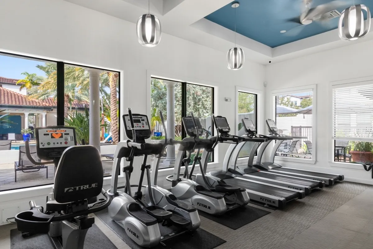 Bright, modern gym at Cottonwood Lighthouse Point Apartments with state-of-the-art exercise equipment and scenic pool views through expansive windows.