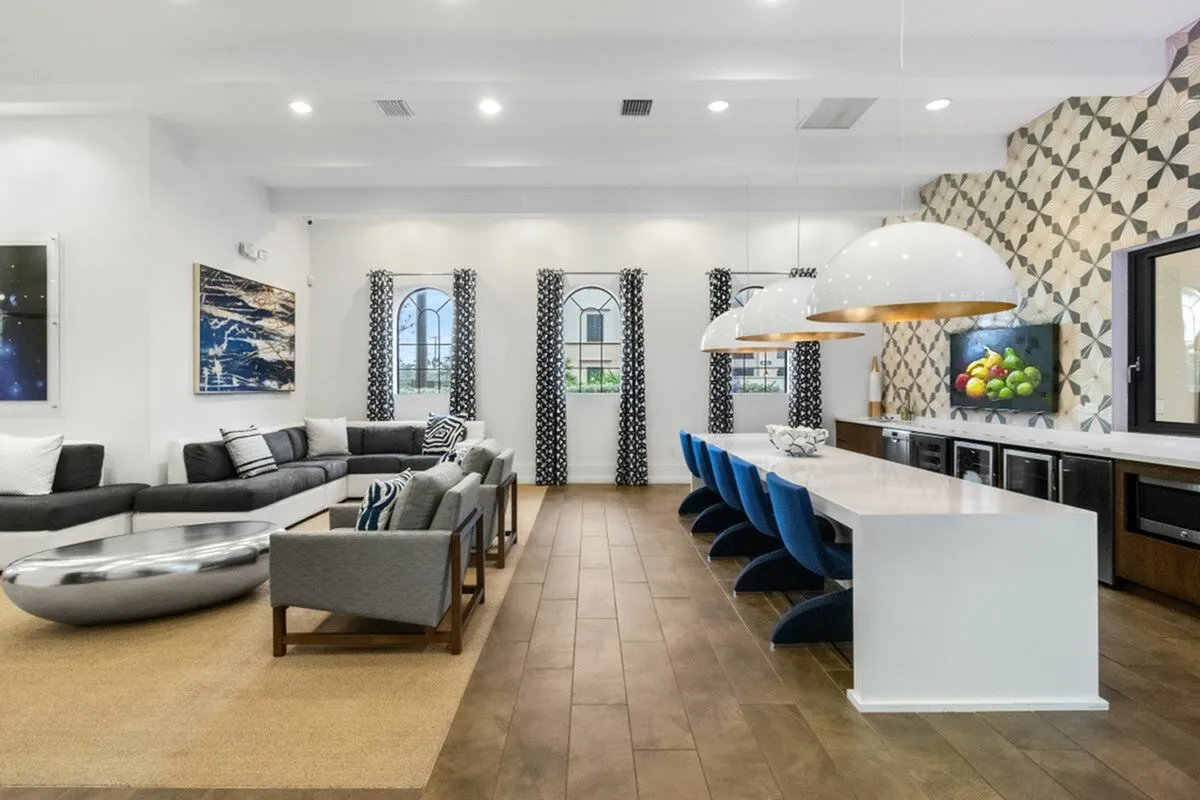 Luxurious clubroom at Cottonwood Lighthouse Point Apartments with modern decor, featuring a sleek white dining table, stylish blue chairs, and elegant lounge seating.