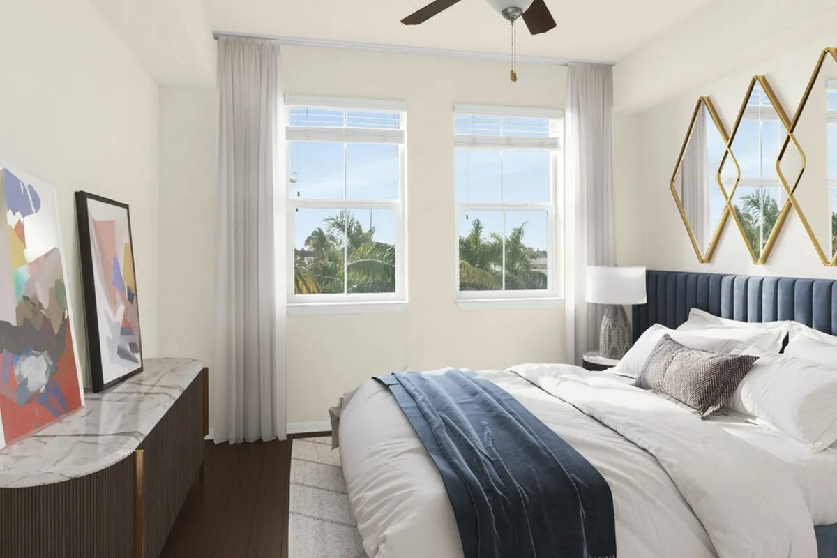 Elegant bedroom at Lighthouse Point Apartments with large windows, plush bedding, contemporary art, and stylish mirror accents, offering serene natural views.