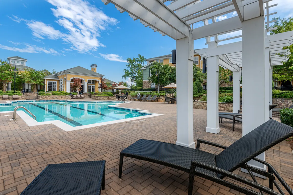 Inviting poolside retreat at Cottonwood Reserve Apartments with modern loungers, surrounded by lush greenery and charming clubhouse.