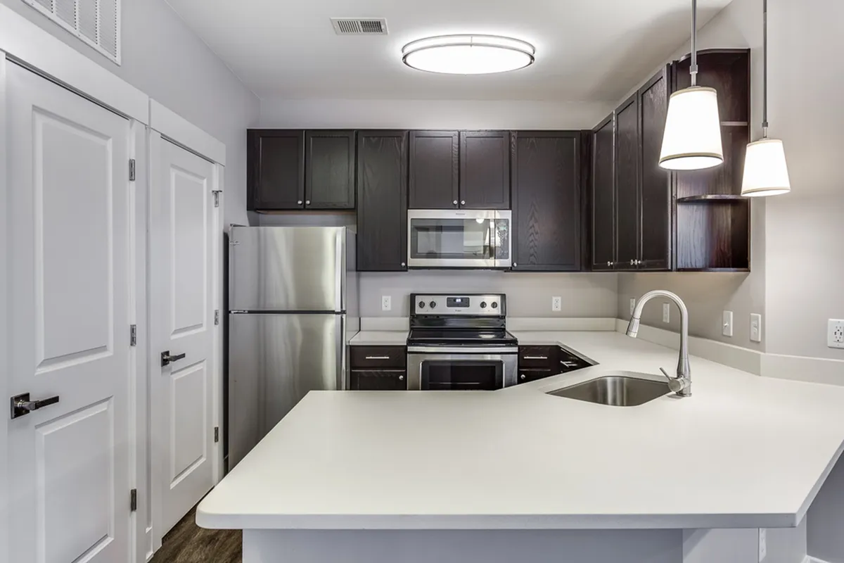 Modern kitchen at Cottonwood Reserve Apartments with sleek dark cabinets, stainless steel appliances, and elegant pendant lighting enhancing a spacious countertop.