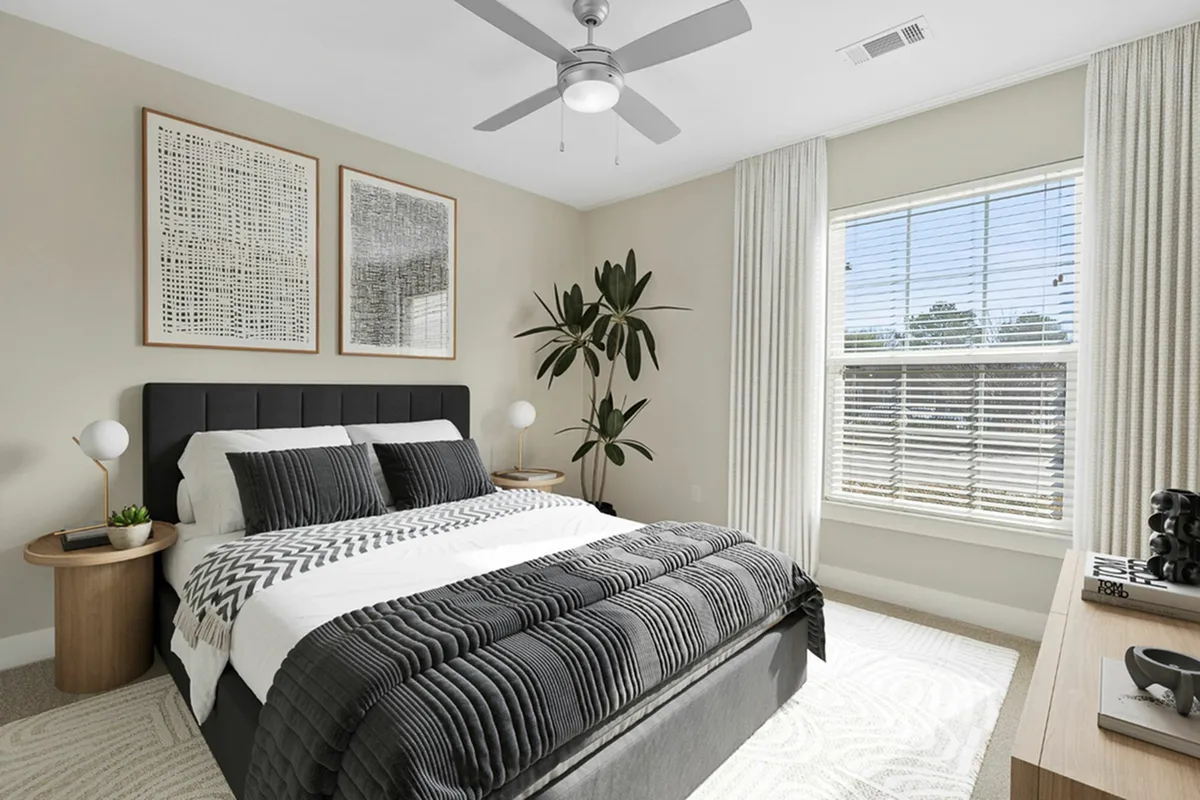 Bright and modern bedroom at Cottonwood Reserve Apartments with a stylish grey bed, elegant artwork, and a sunny window view, perfect for relaxation.