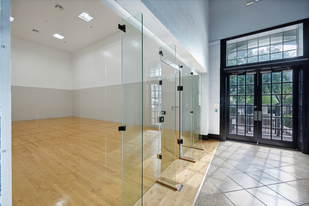 Elegant racquetball court at Cottonwood Ridgeview Apartments with polished wooden flooring and glass walls next to large, sunlit double doors.