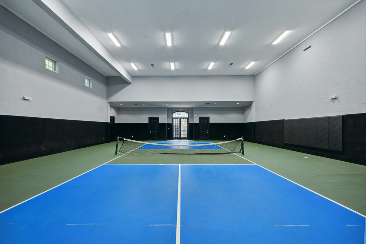 Spacious indoor pickleball court at Cottonwood Ridgeview Apartments with a vibrant blue tennis court, high ceilings, and modern lighting, offering a perfect space for active recreation.
