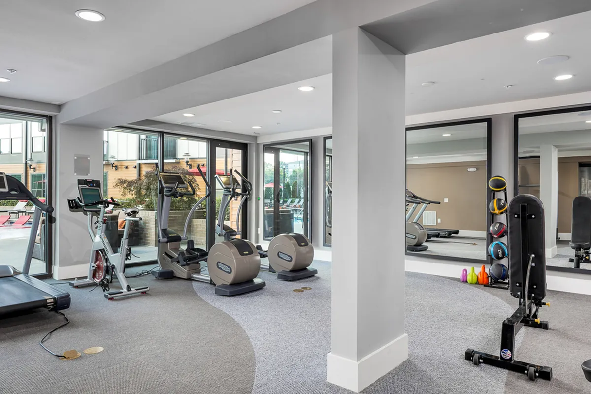 Modern apartment gym at Cottonwood Westside with state-of-the-art treadmills, exercise bikes, and free weights, surrounded by large mirrors and natural light.