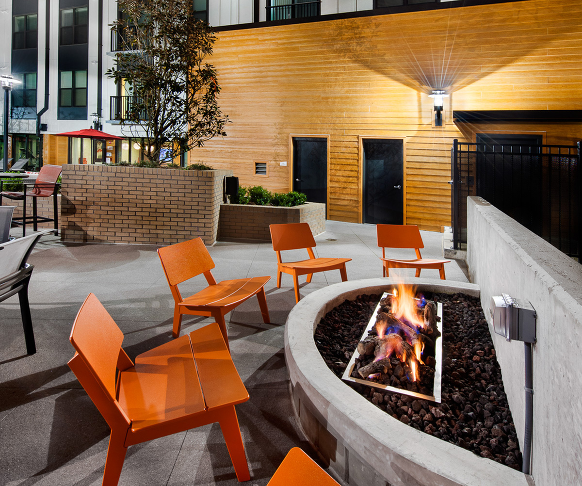 Inviting outdoor lounge area at Cottonwood Westside Apartments featuring modern orange chairs and a warm, glowing fire pit, perfect for evening gatherings.
