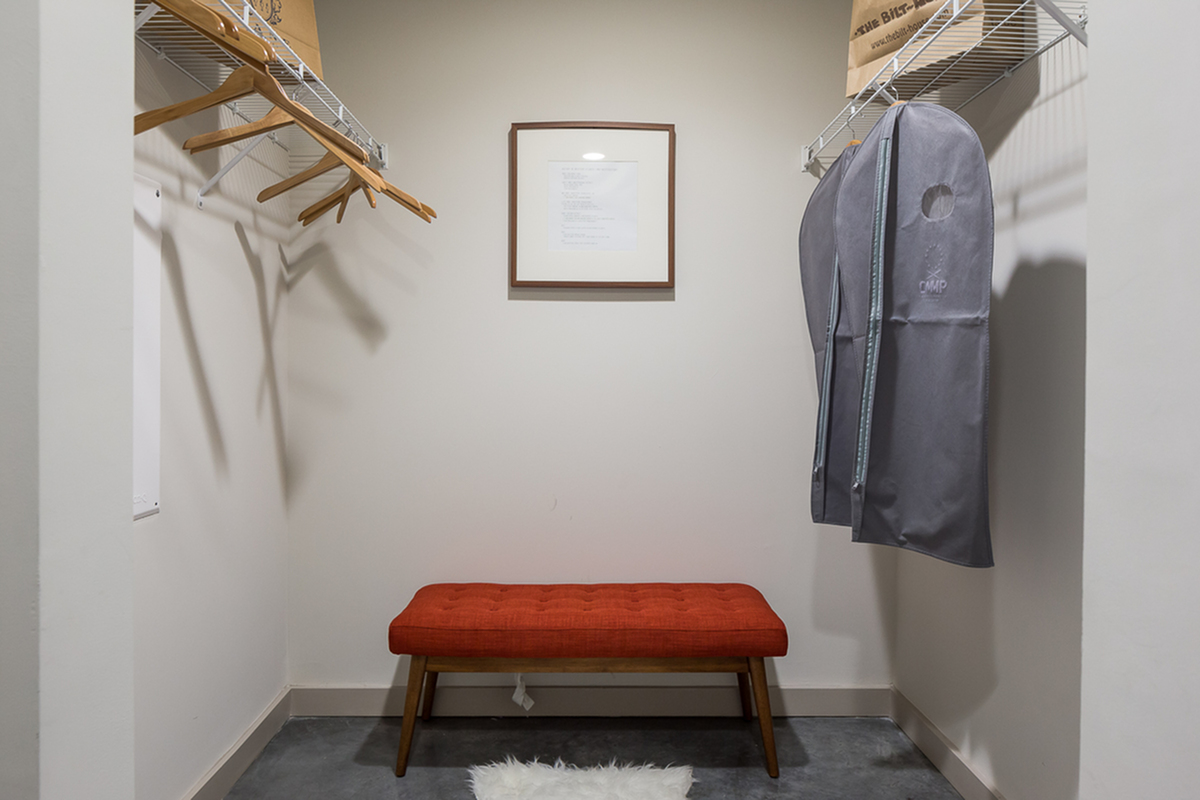 Spacious walk-in closet at Cottonwood Westside Apartments featuring a modern orange bench, ample shelving for storage, and a cozy rug.