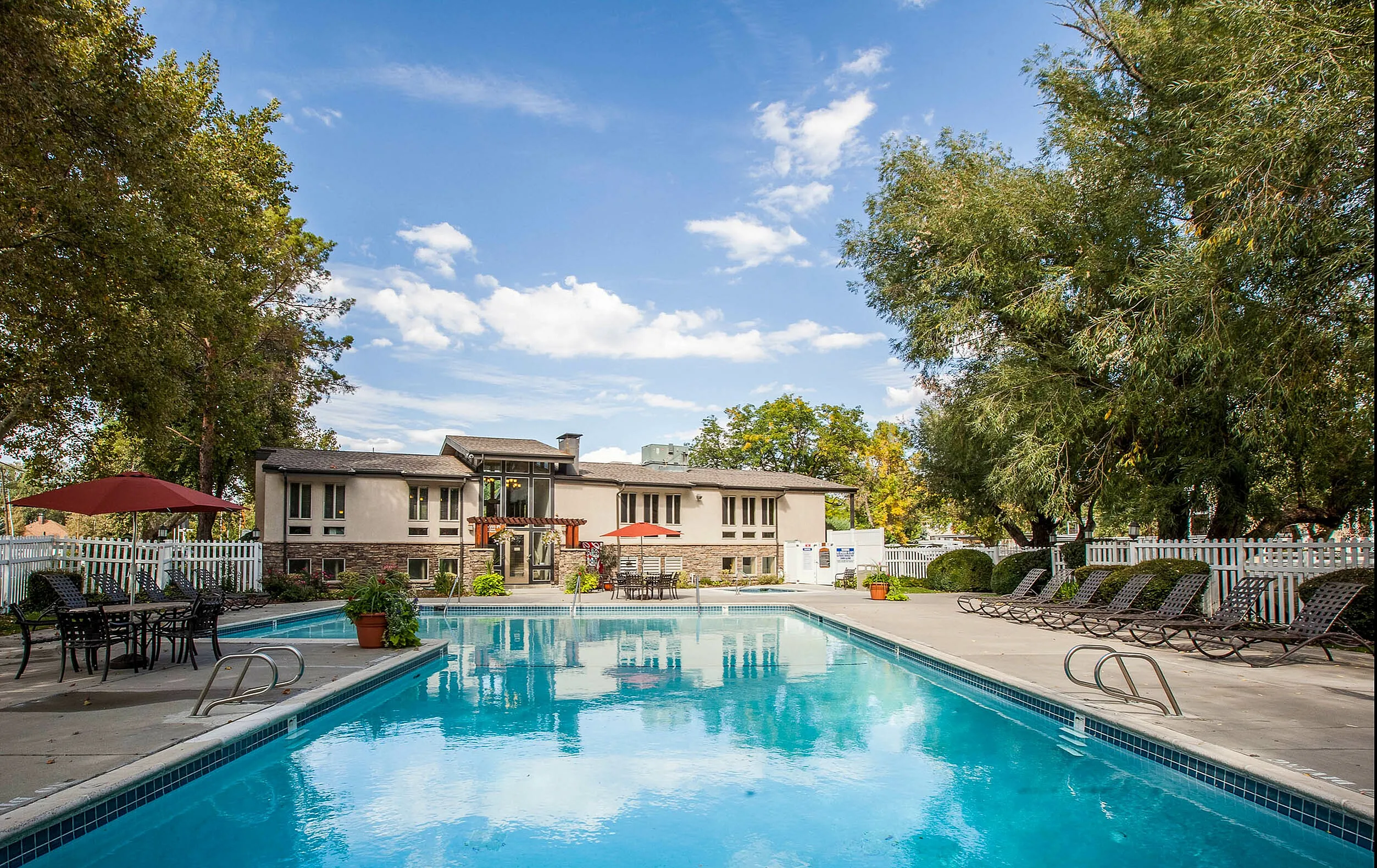 Inviting outdoor pool area at Fox Point in Old Farm Apartments with modern lounge chairs and sun umbrellas, surrounded by lush greenery for a serene atmosphere.