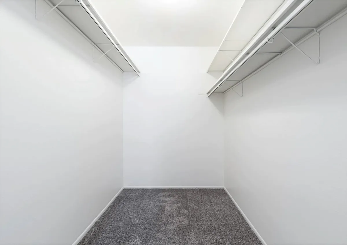 Spacious walk-in closet at Fox Point in Old Farm Apartments with dual shelving, perfect for organized storage, featuring plush carpet and sleek white walls.