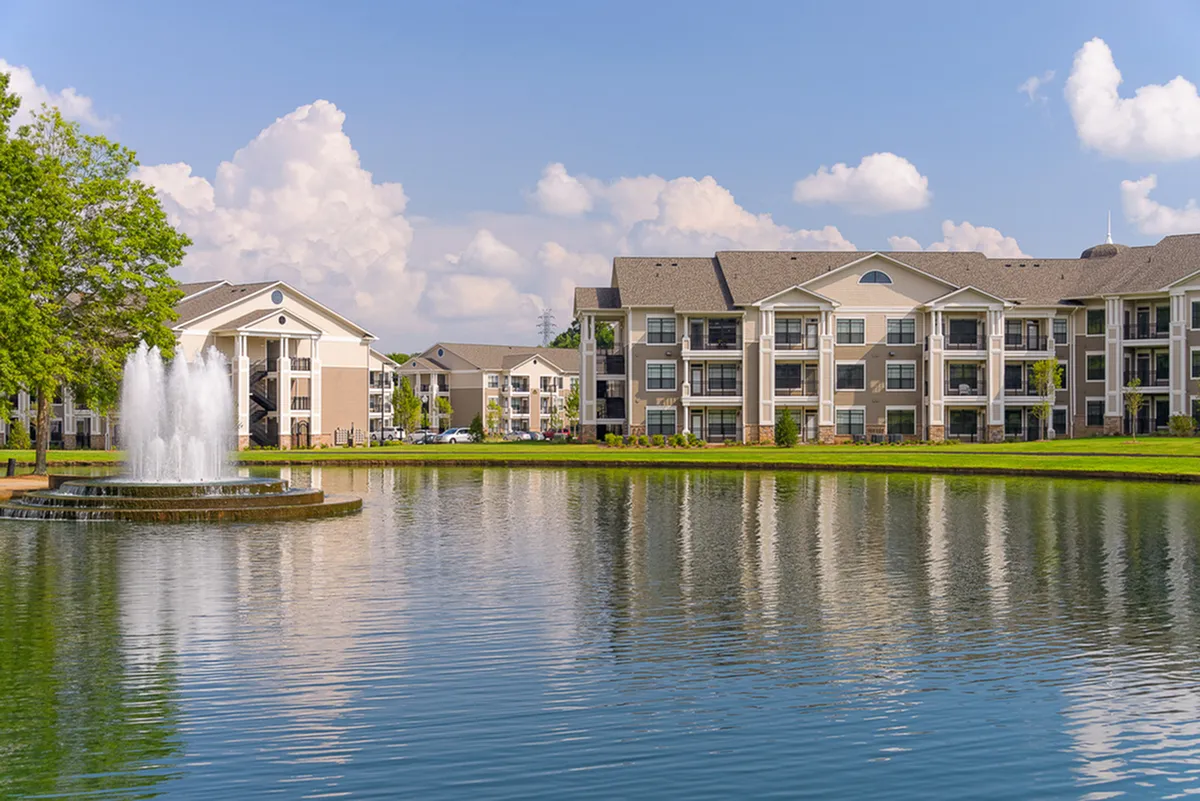 Elegant apartment complex, Heights at Meridian, with a scenic pond and fountain in the foreground, surrounded by lush greenery under a clear blue sky.