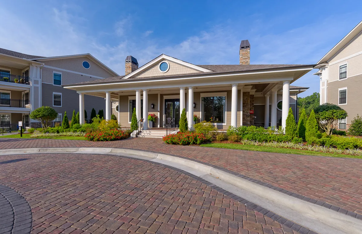 Elegant apartment building, Heights at Meridian, with a grand entrance featuring tall white columns, surrounded by lush landscaping and vibrant flowers under a clear blue sky.