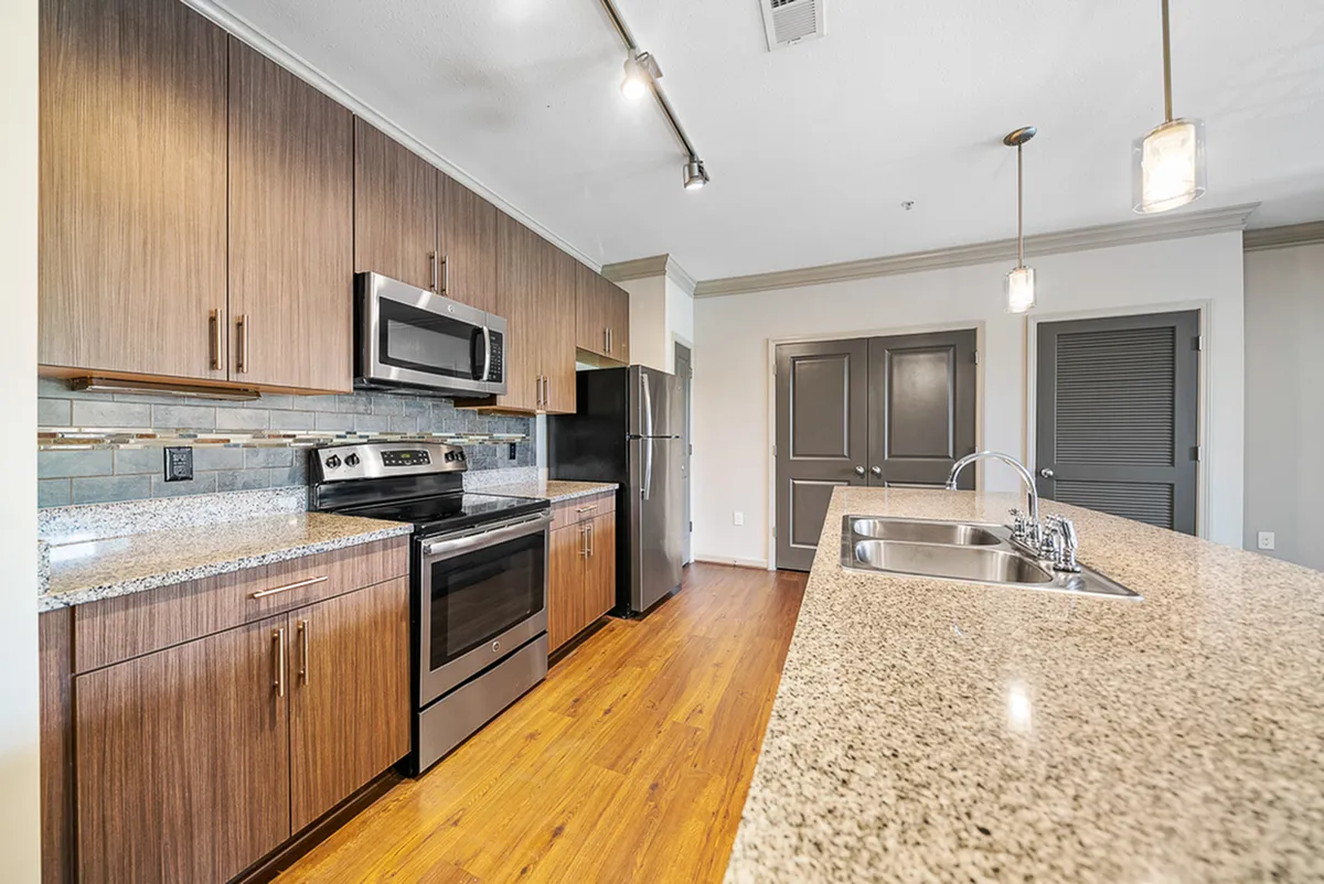 Sleek modern kitchen at Heights at Meridian Apartments with granite countertops, stainless steel appliances, and warm wood cabinetry illuminated by stylish pendant lighting.
