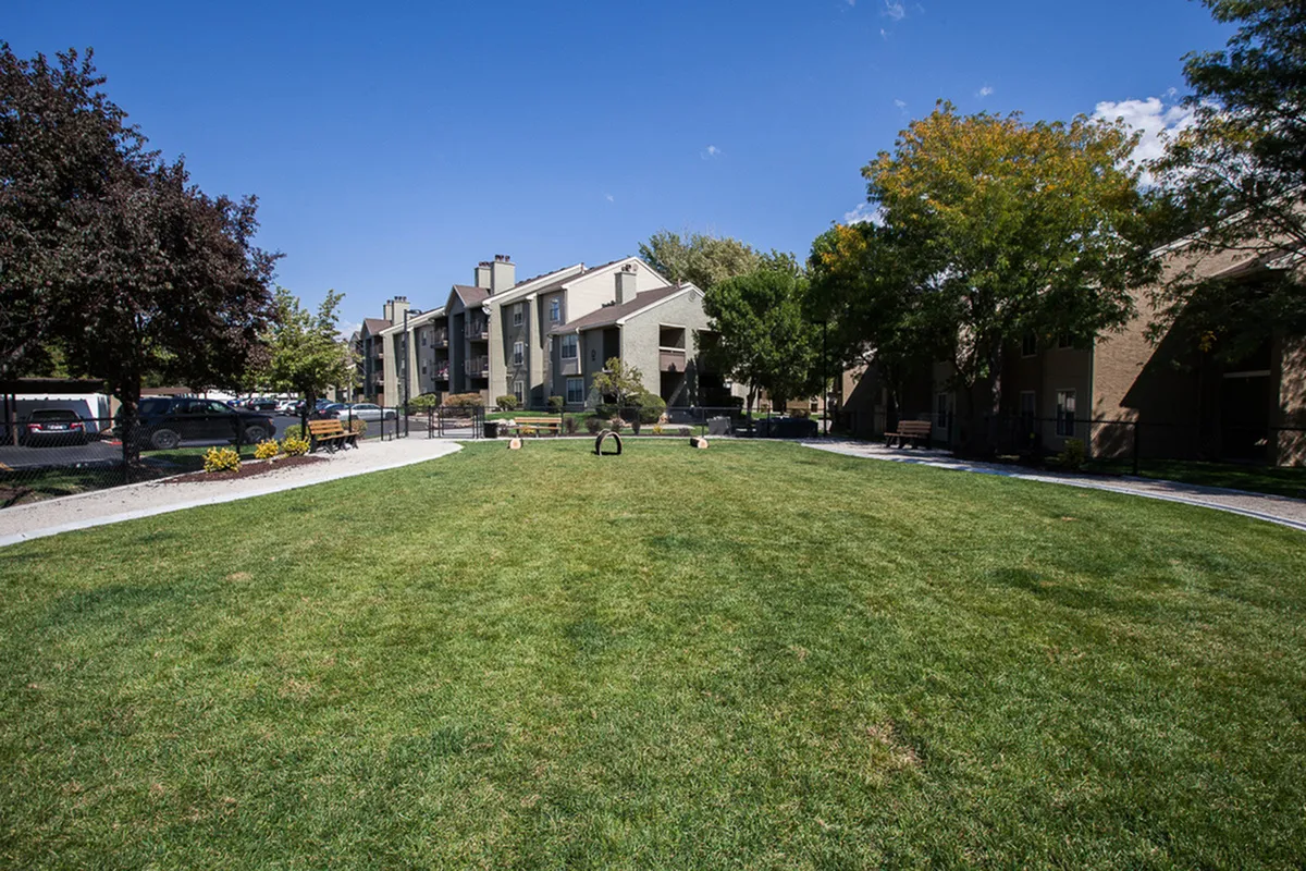 Charming apartment community with lush green lawns, mature trees, and contemporary architecture under a clear blue sky.