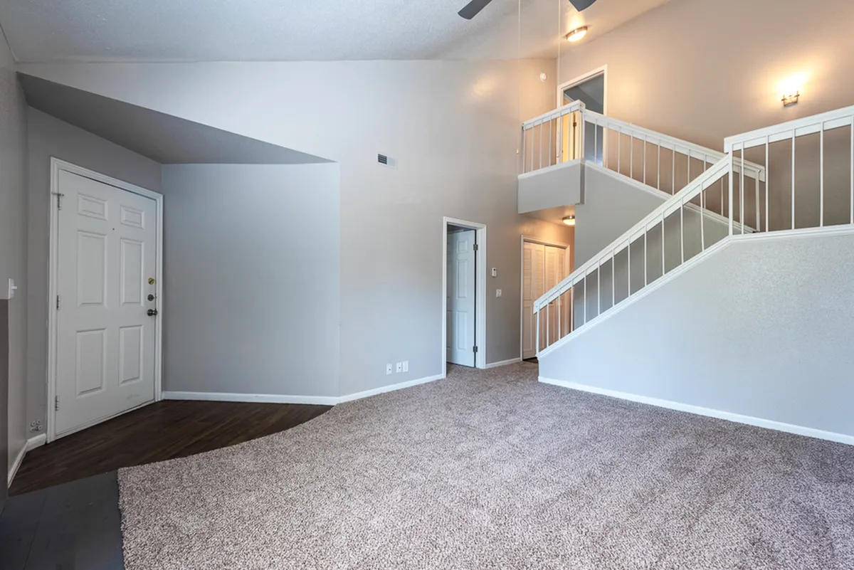 Bright and inviting living space with high ceilings, cozy carpeted floors, and elegant white railing staircase.