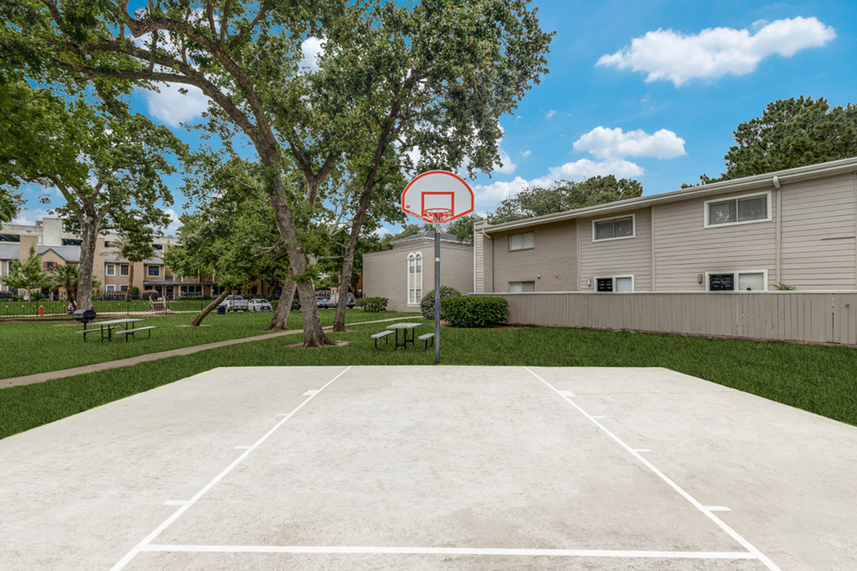 Charming apartment courtyard with a vibrant basketball court, shaded by mature trees and surrounded by cozy residences, perfect for community fun.