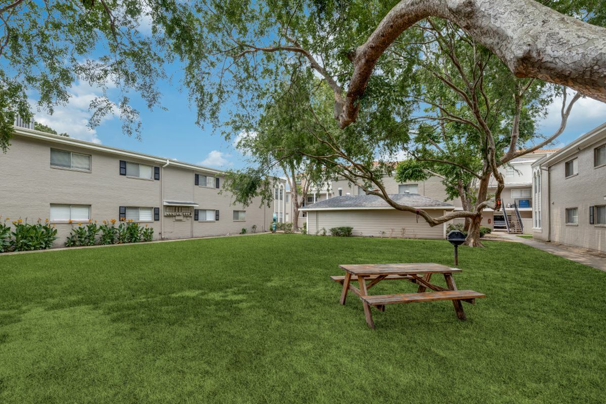 Charming apartment courtyard featuring lush green grass, a picnic table, and vibrant landscaping, creating a perfect outdoor retreat.