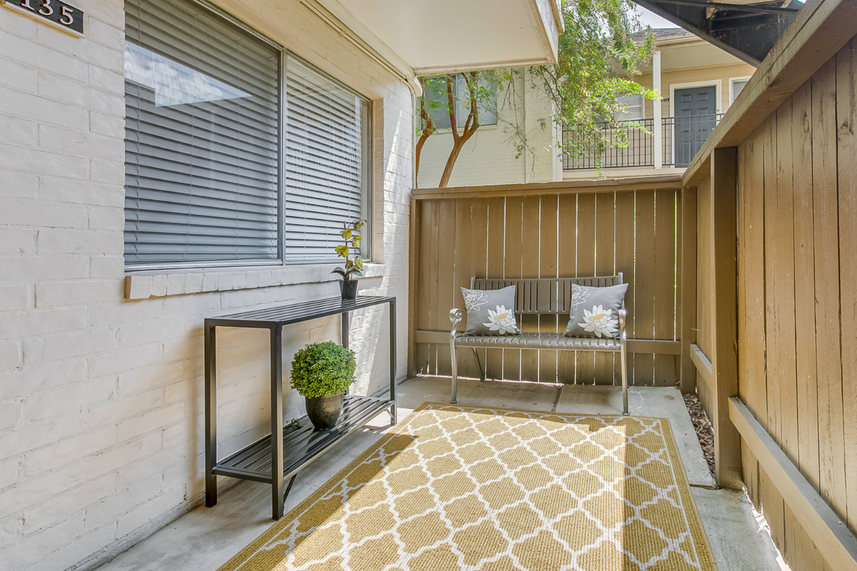 Inviting outdoor patio featuring elegant seating with plush floral cushions, a decorative side table, and lush greenery.