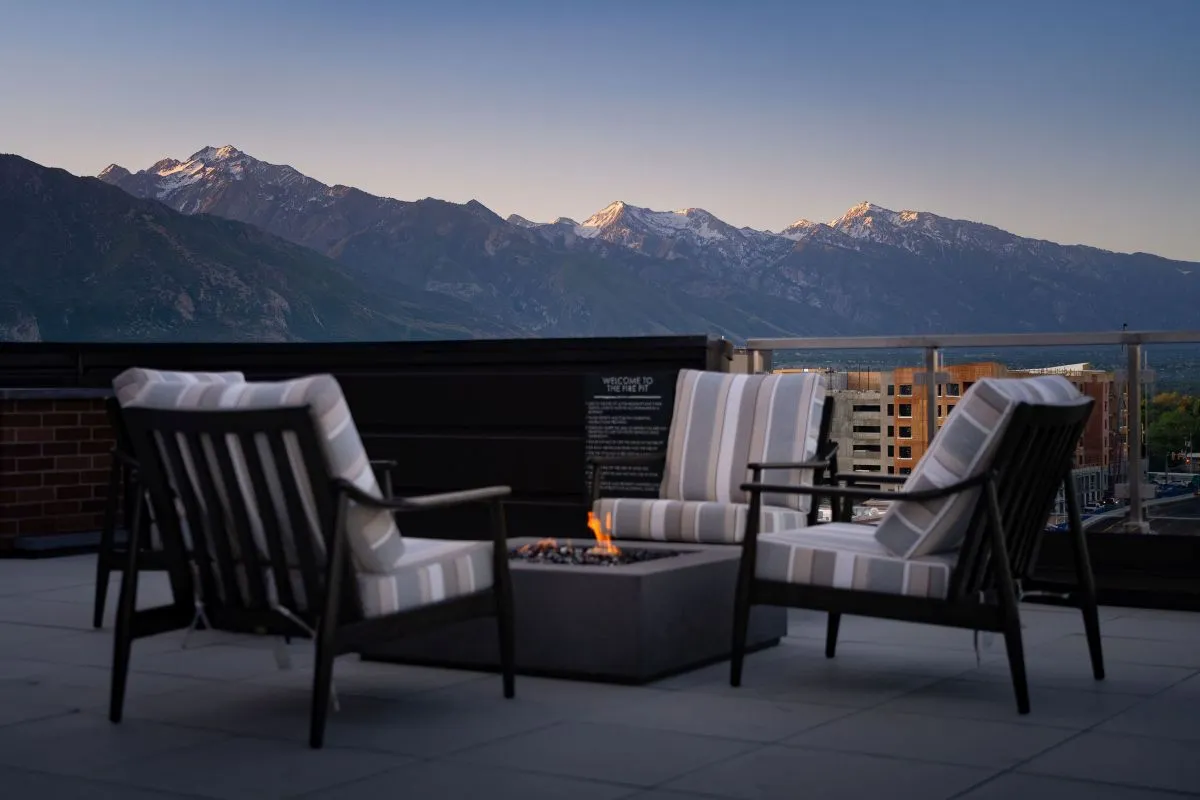 Luxurious rooftop lounge with cozy armchairs around a fire pit, offering breathtaking mountain views at sunset at The Richmond Apartments in Millcreek Utah