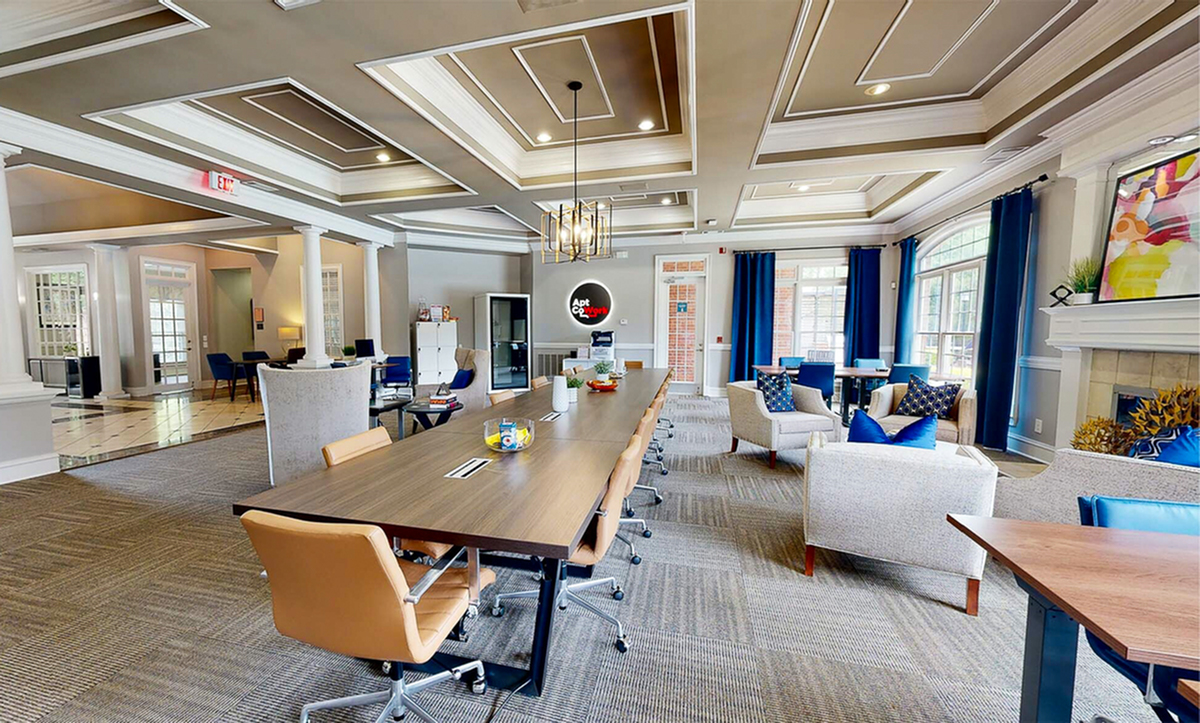 Elegant coworking space at Retreat at Peachtree City Apartments with modern decor features a long communal table, cozy seating, and natural light from large windows.
