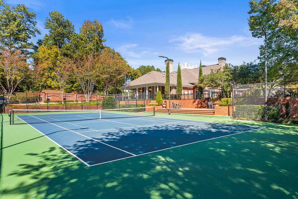 Beautifully maintained tennis court surrounded by lush greenery and modern clubhouse in a serene residential setting.