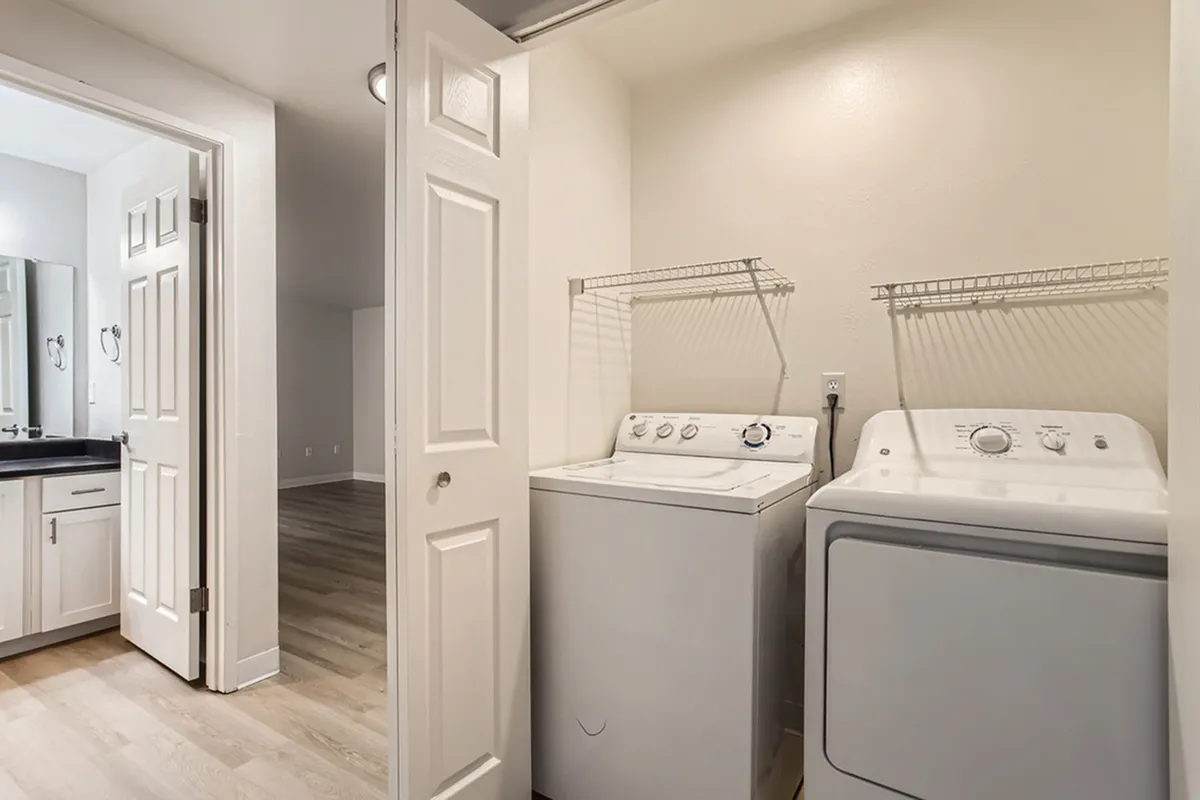 Sleek laundry area with washer and dryer, featuring modern shelving and adjacent bathroom entry.